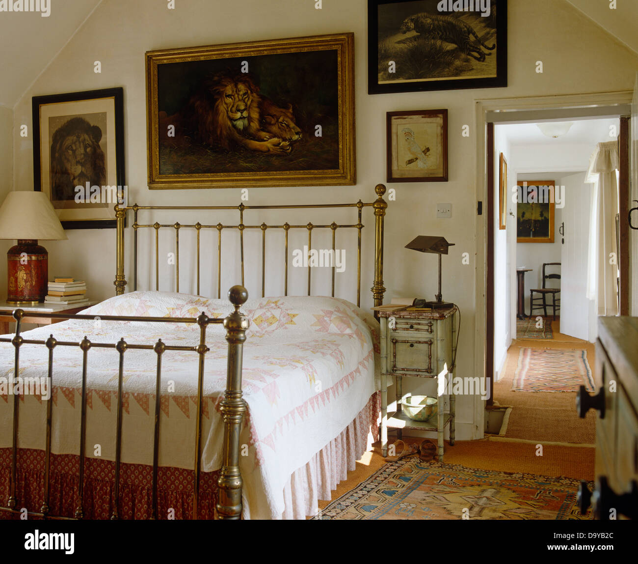 Dipinti di leoni sulla parete sopra il letto in ottone con bianco e rosa trapunta nel paese camera da letto con porta aperta all'atterraggio Foto Stock