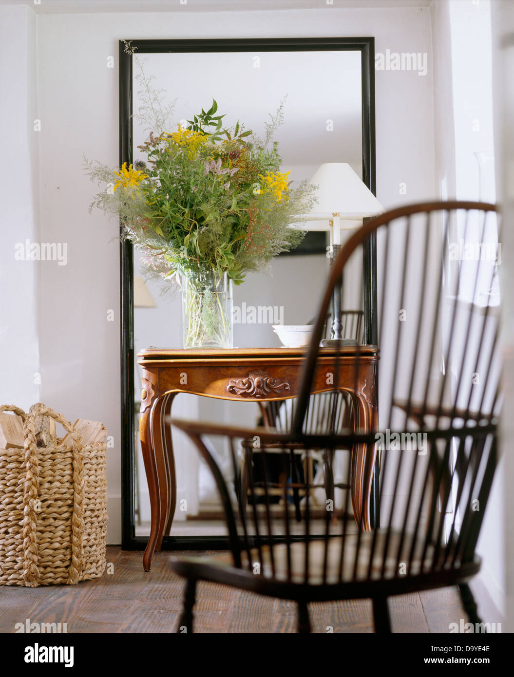 Sedia di Windsor in bianco cottage soggiorno con fiori e la lampada bianca sul tavolo antico davanti a uno specchio grande Foto Stock