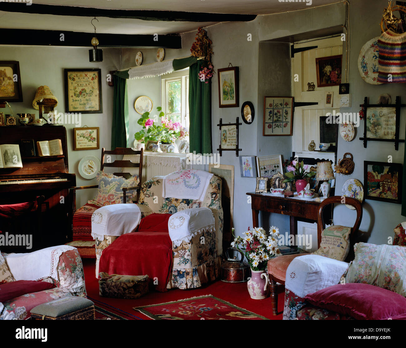 Antimacassars bianco sulla poltrona floreale in cottage ingombra la stanza di seduta con il pianoforte e gruppi di piccole immagini Foto Stock