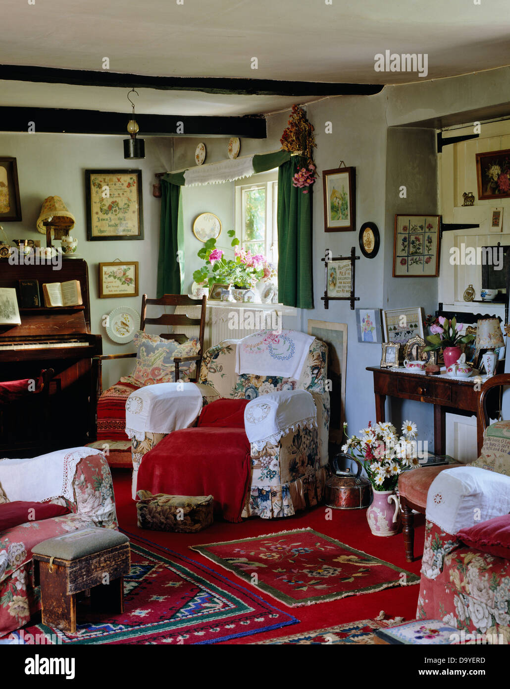 Antimacassars bianco sulla poltrona floreale in cottage ingombra la stanza di seduta con il pianoforte e coloratissimo tappeto rosso Foto Stock