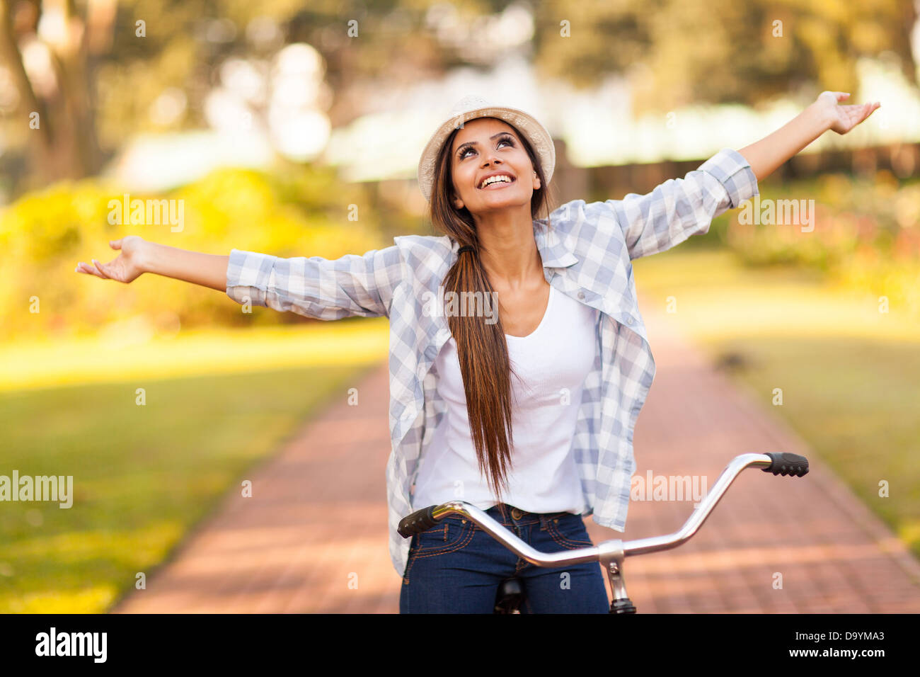 Piuttosto giovane donna godendo di bicicletta equitazione presso il parco con le braccia aperte Foto Stock