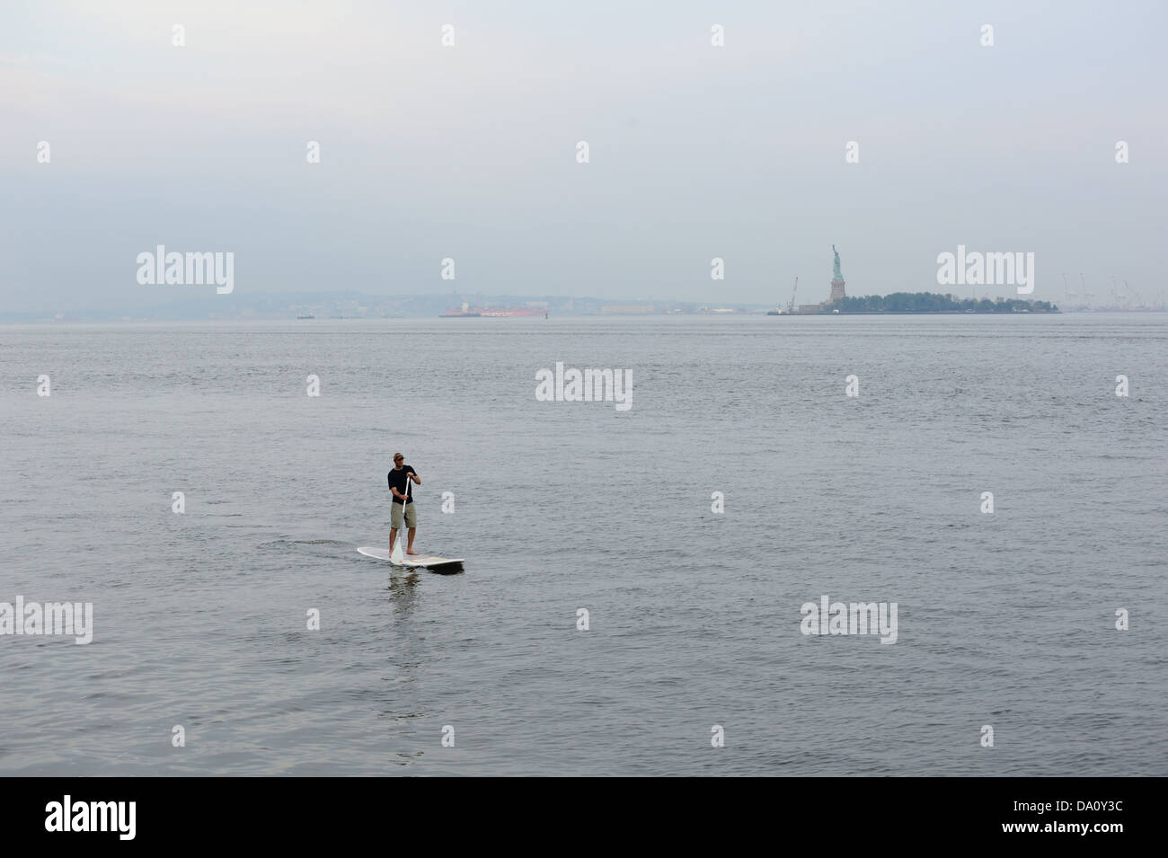 Un uomo stand-up paddling sul fiume Hudson in New York City con la Statua della Libertà in background. Foto Stock