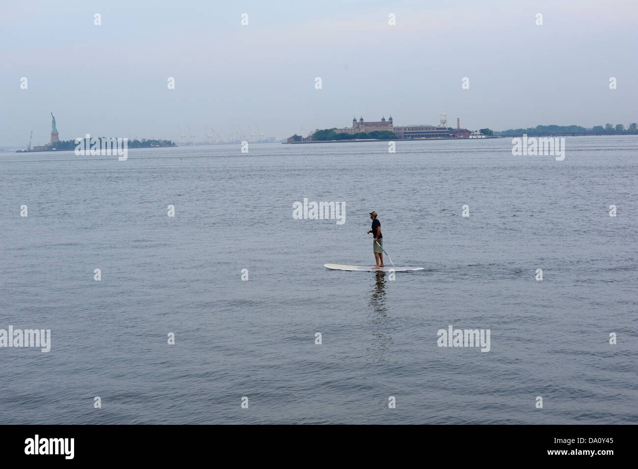 Un uomo stand-up paddling sul fiume Hudson in New York City vicino a Ellis Island e Liberty Island. Foto Stock