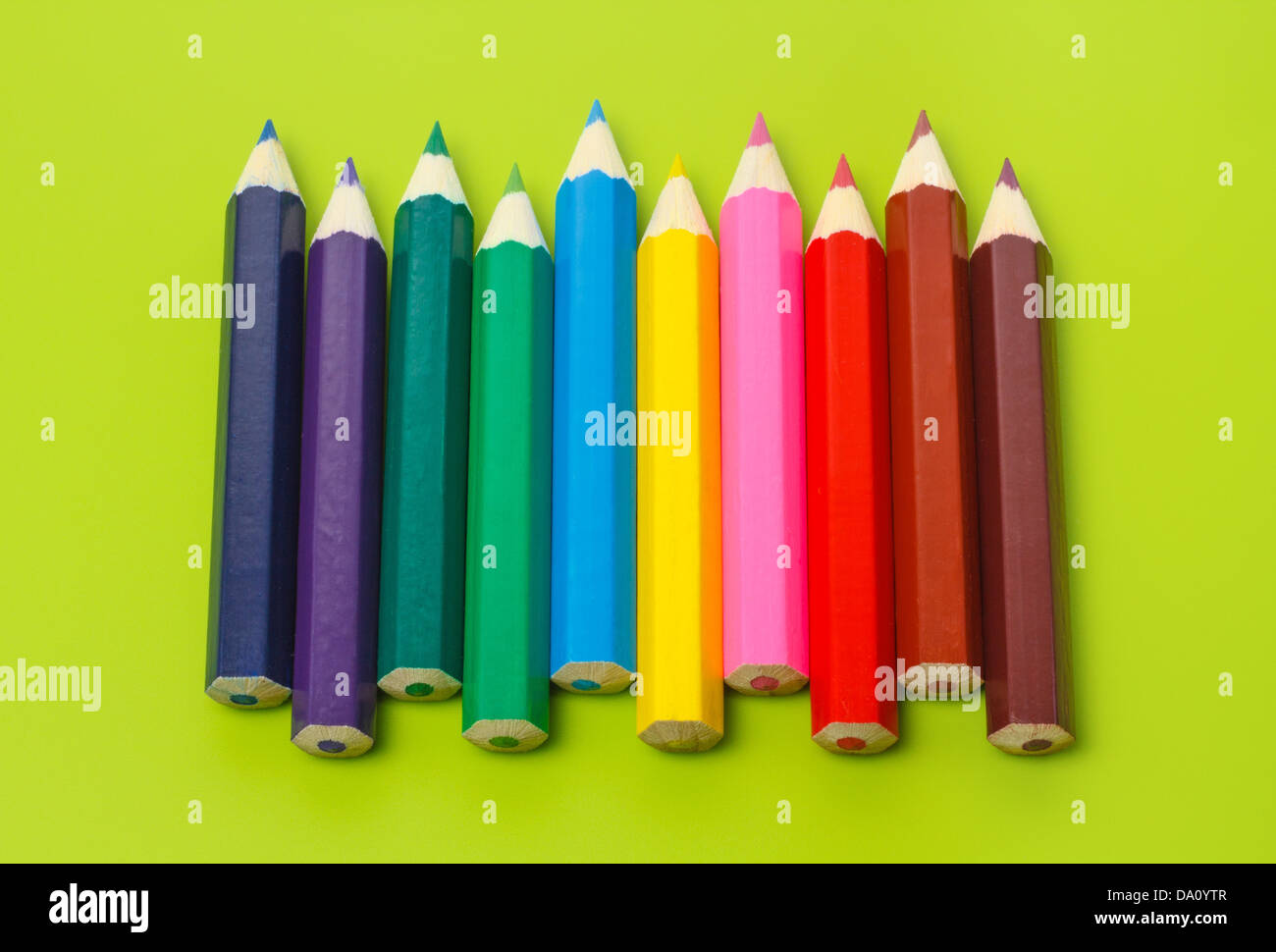 Piccole matite colorate in una fila in arcobaleno di colori contro il fondo color verde oliva Foto Stock
