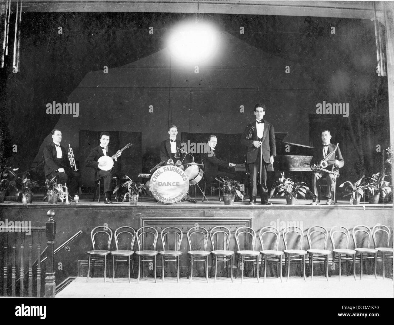 Fotografia in bianco e nero del gruppo da ballo Cyril Fairman che si pone con strumenti su un palco con una fila di sedie in legno davanti, intorno al 1920. Foto Stock