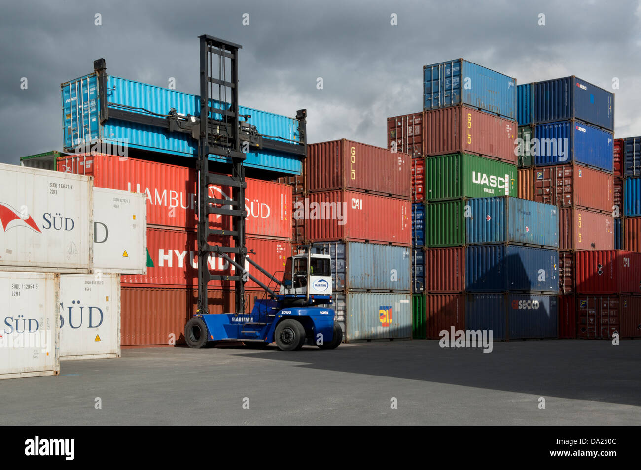 Un veicolo di sollevamento solleva un contenitore a partire da una pila di altri in Trafford Park vicino a Manchester (solo uso editoriale). Foto Stock