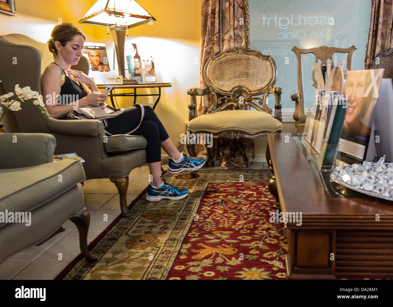 Una paziente femmina gioca con il suo smart phone mentre erano in attesa in una cura della pelle bellezza facility in sala d'attesa. Stati Uniti d'America. Foto Stock