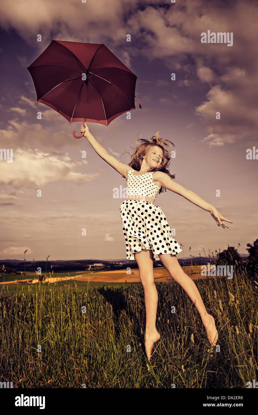 Teen girl jumping con un ombrello nella parte anteriore del paesaggio rurale Foto Stock