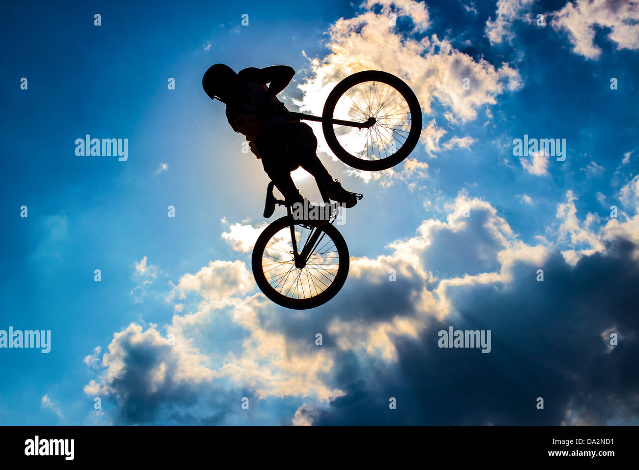 Silhouette di un ciclista battenti in uno sfondo di sole e cielo blu con nuvole Foto Stock