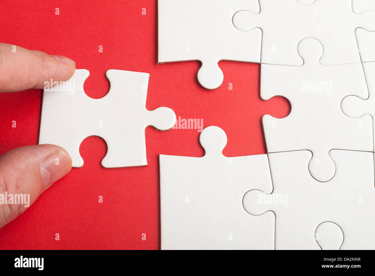 Mano azienda pezzo di puzzle e di inserirlo nel gruppo del libro bianco i puzzle Foto Stock