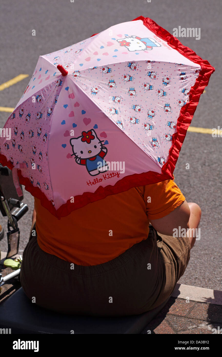 Donna riparo dal sole sotto Hello Kitty ombrello a Poole, Dorset in giugno Foto Stock