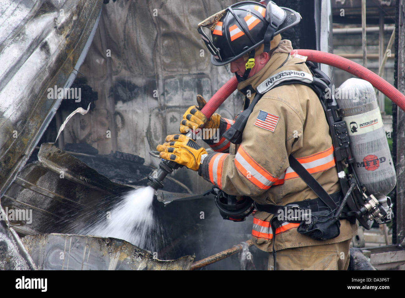 Un vigile del fuoco usando un hoseline per estinguere un hot spot in una scena di fuoco Foto Stock