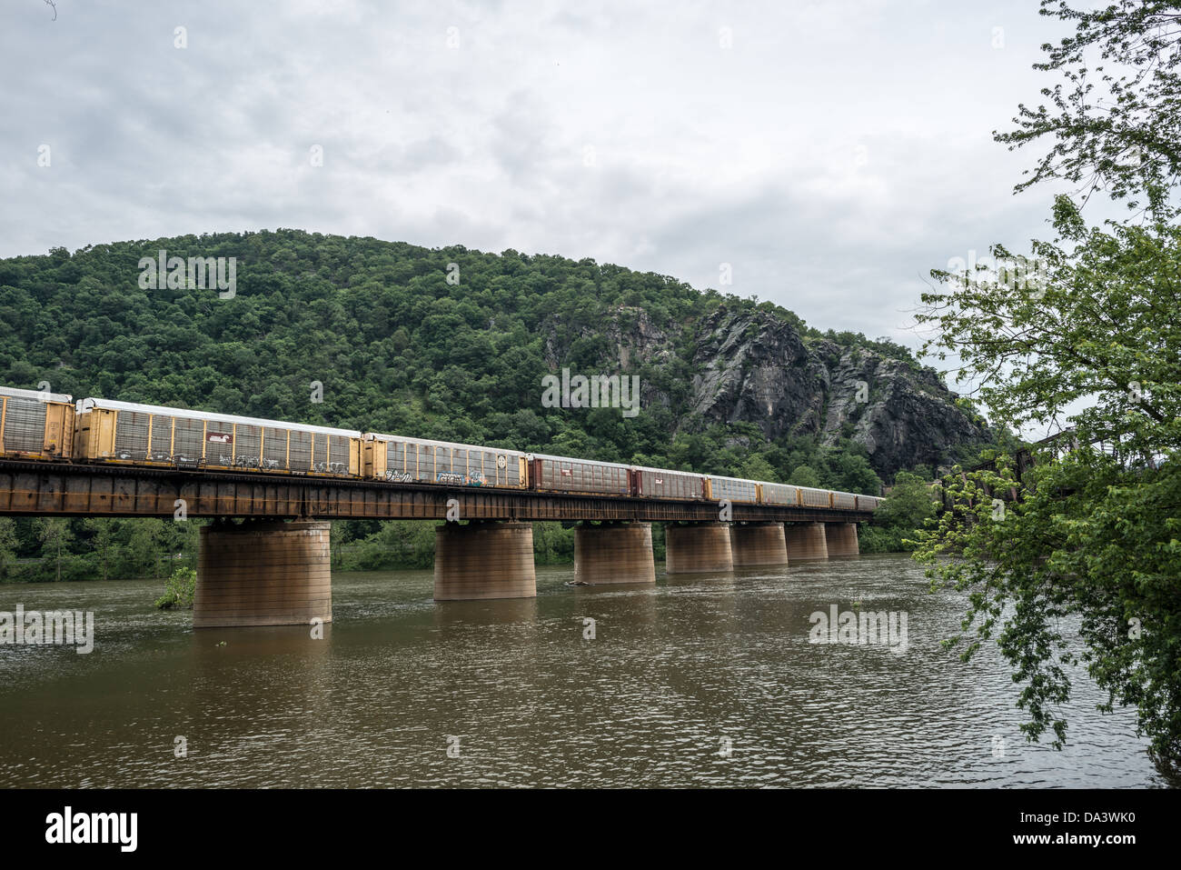 HARPERS FERRY, West Virginia, Stati Uniti — Un treno merci attraversa lo storico ponte ferroviario sul fiume Potomac a Harpers Ferry. Questa ferrovia attiva, sullo sfondo delle Blue Ridge Mountains, dimostra la continua importanza di Harpers Ferry come centro di trasporto, che mescola infrastrutture del XIX secolo con il commercio moderno. Foto Stock