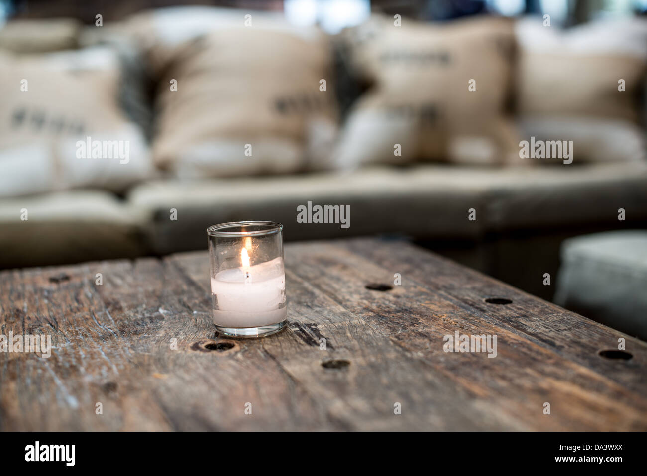 Una piccola candela votiva ssits su una tavola in legno rustico in un ristorante bar nella parte anteriore di un divano. Foto Stock