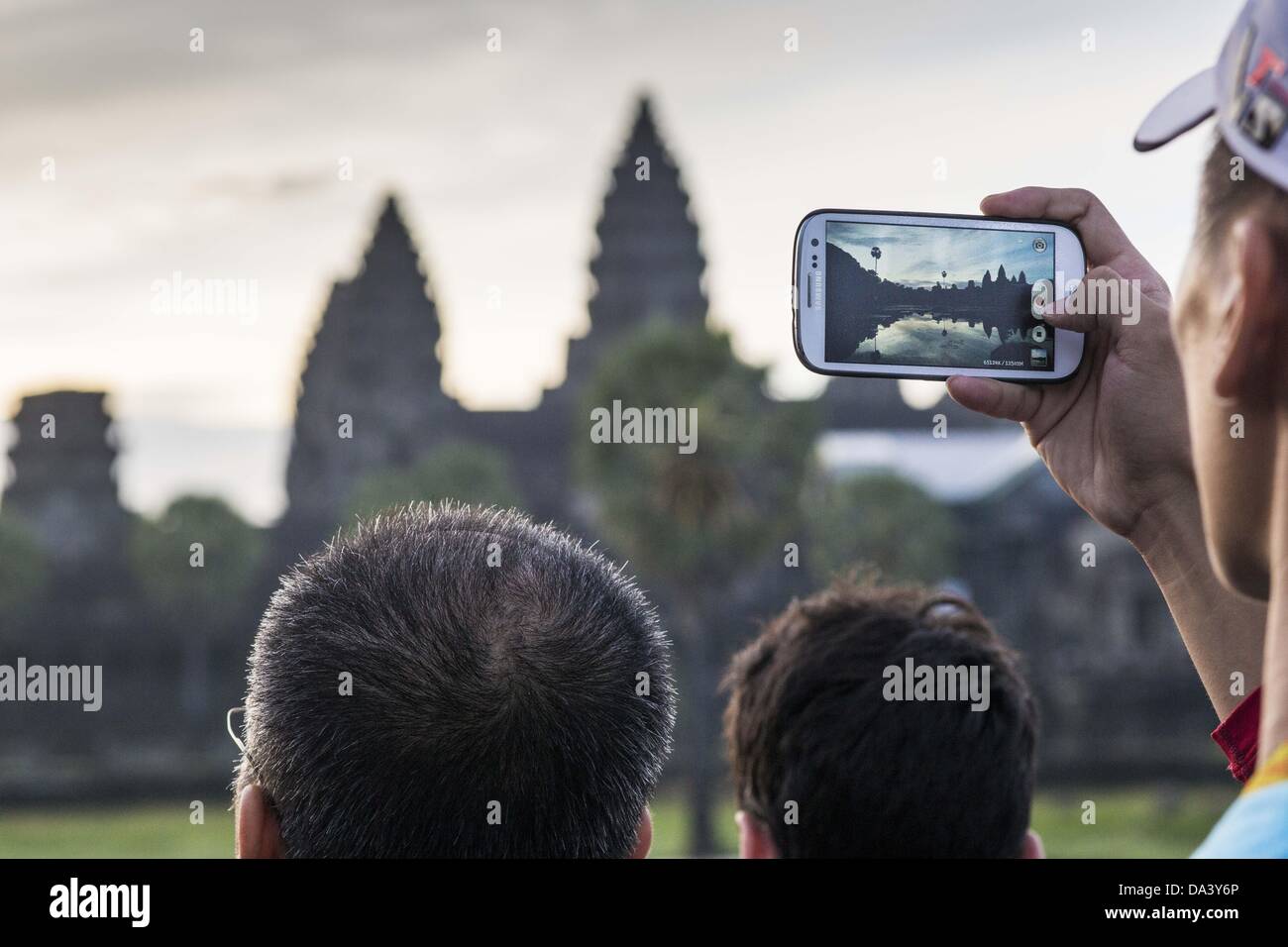 2 luglio 2013 - Siem Reap, Siem Reap, Cambogia - un turista fotografie il sorgere del sole con il suo smart phone a Angkor Wat. Angkor Wat è il tempio più grande complesso nel mondo. Il tempio fu costruito dal re Khmer Suryavarman II nei primi anni del XII secolo in Yasodharapura (oggi Angkor), la capitale dell'Impero Khmer, come suo tempio di stato ed eventuali mausoleo. Angkor Wat è stata dedicata a Vishnu. È il meglio preservato tempio presso il sito, ed è rimasto un centro religioso sin dalla sua fondazione â€" Primo indù, poi buddista. Il tempio si trova nella parte superiore dell'alto stile classico di Khm Foto Stock