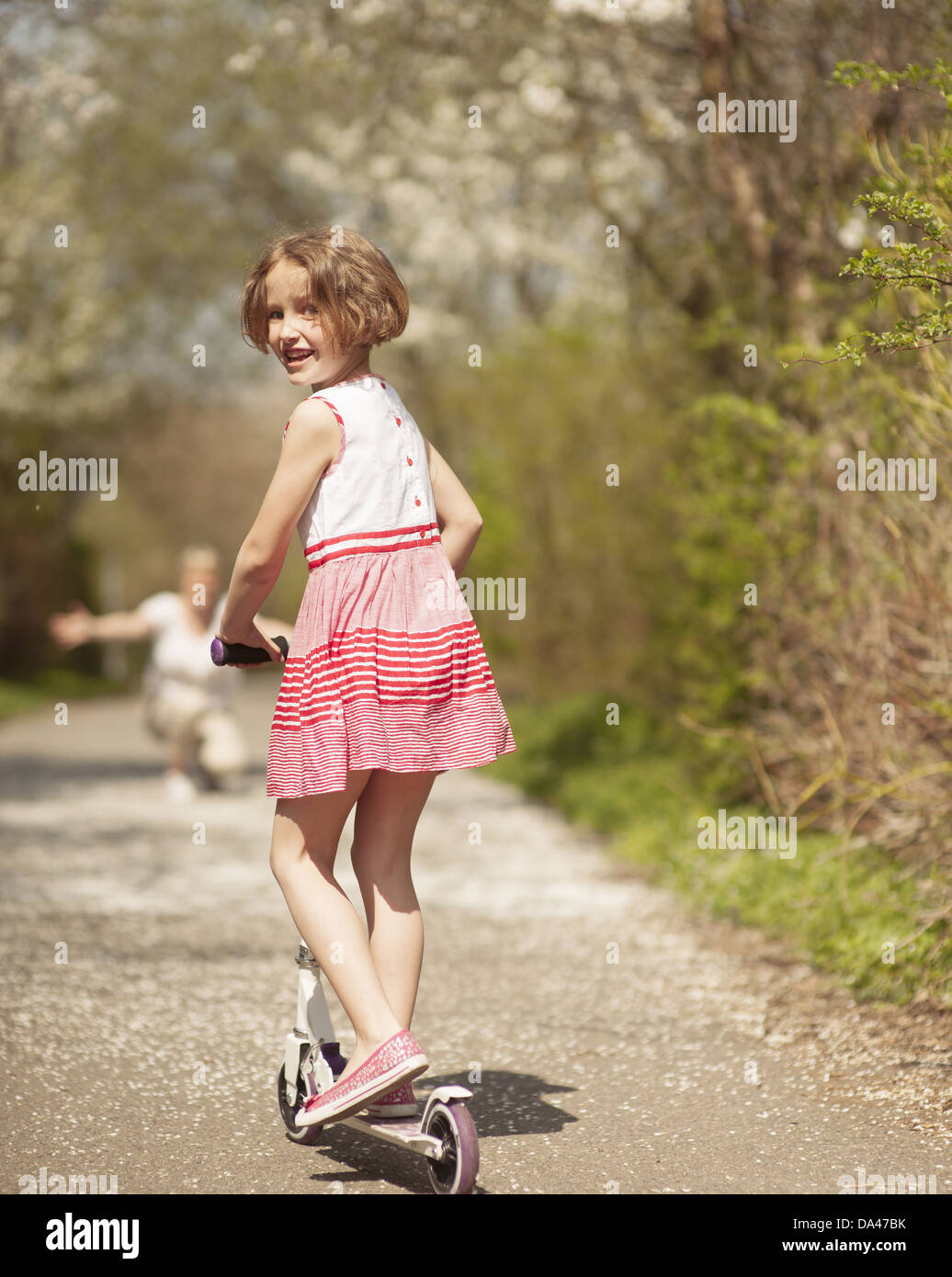 Ragazza giovane riding scooter a parcheggiare lontano dalla fotocamera alla madre Foto Stock