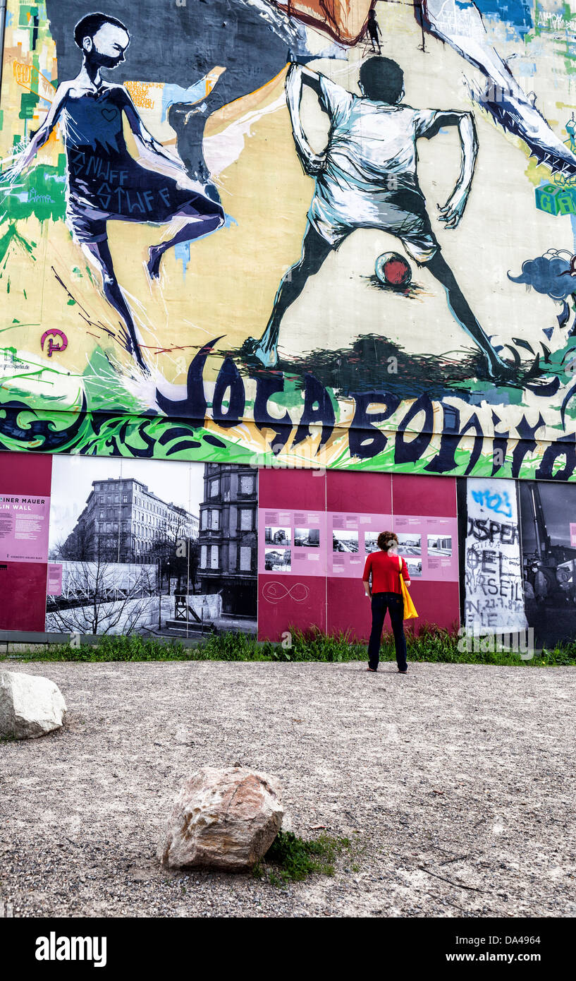 Donna che guarda al Memoriale del Muro di Berlino information board davanti a una parete con Joga bonita (play) splendidamente wall art Foto Stock