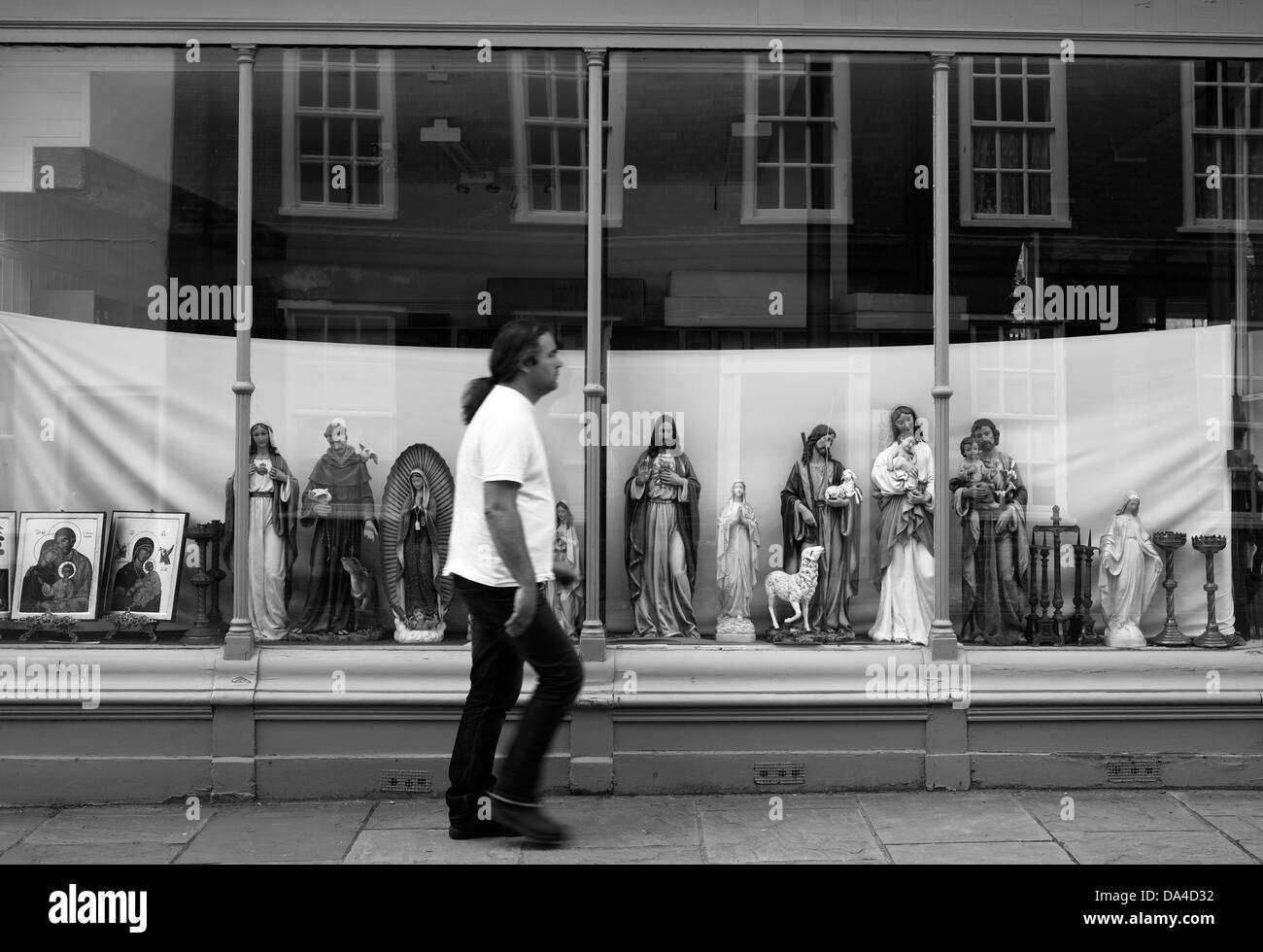 Statue religiose sulla visualizzazione in una finestra del negozio come un uomo cammina passato. Foto Stock