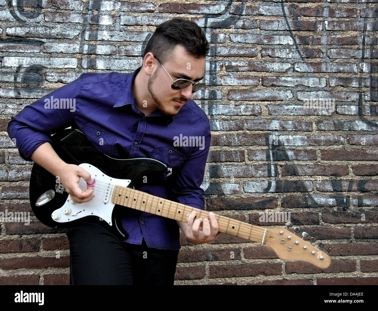Musicista in posa con la sua chitarra in una parete di graffiti Foto Stock