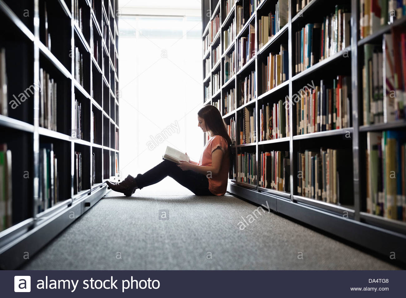 Studentessa seduta sul pavimento della libreria al college campus Foto Stock
