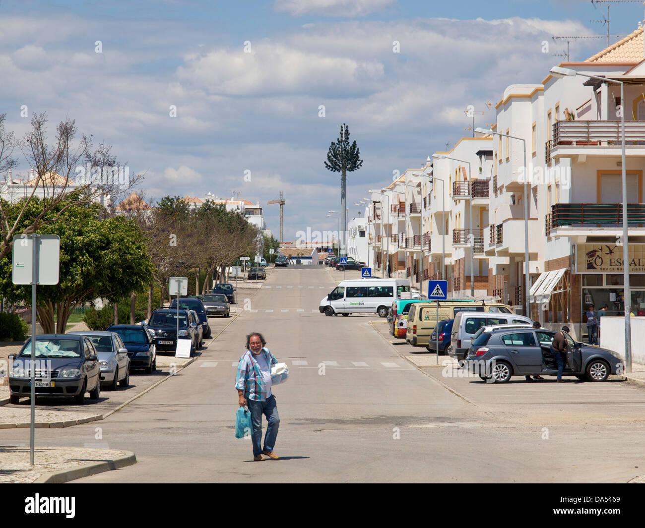 Scena di strada in Cabanas de Tavira, Algarve, Portogallo con l uomo che trasportano prodotti alimentari e antenna cellulare dissimulata come un albero. Foto Stock