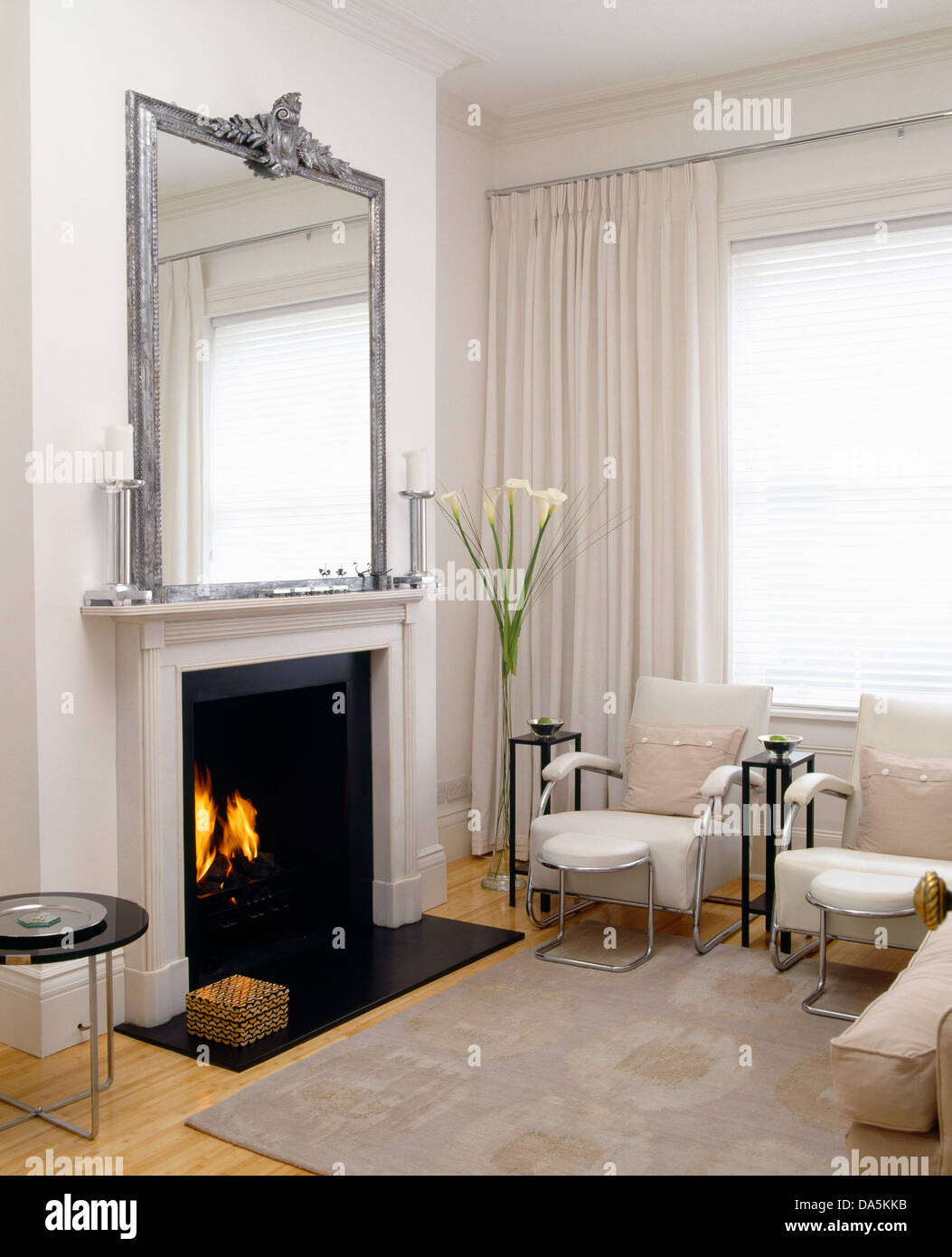 Specchio argento sopra il camino con il fuoco acceso in bianco moderno  salotto con tappeto grigio e bianco+sedie cromate Foto stock - Alamy