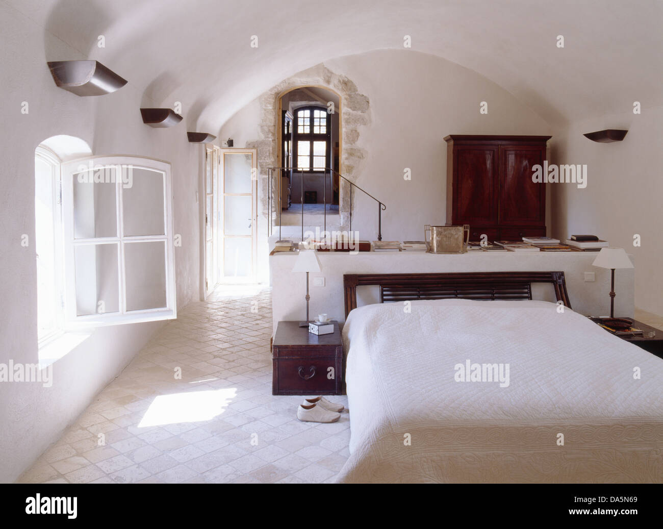 Bianco con pavimenti piastrellati in ceramica nella luminosa e ariosa e paese francese camera con piccole lampade su tavole montate su entrambi i lati del letto matrimoniale Foto Stock