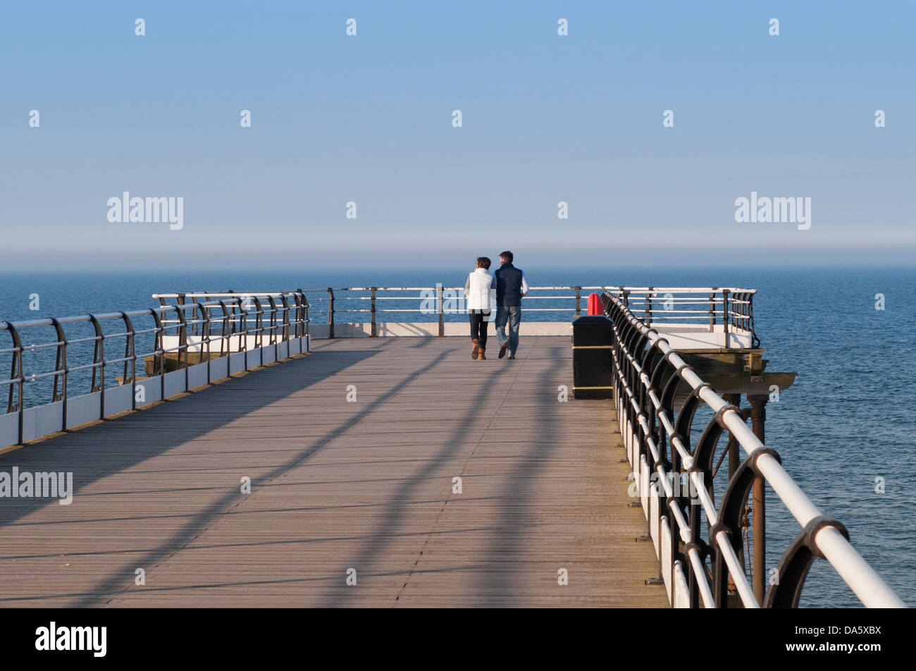 Sole Blu serata estiva sky & vista del giovane a camminare insieme sulla quieta scenic molo sul mare oltre il mare calmo - Cambs, England, Regno Unito Foto Stock