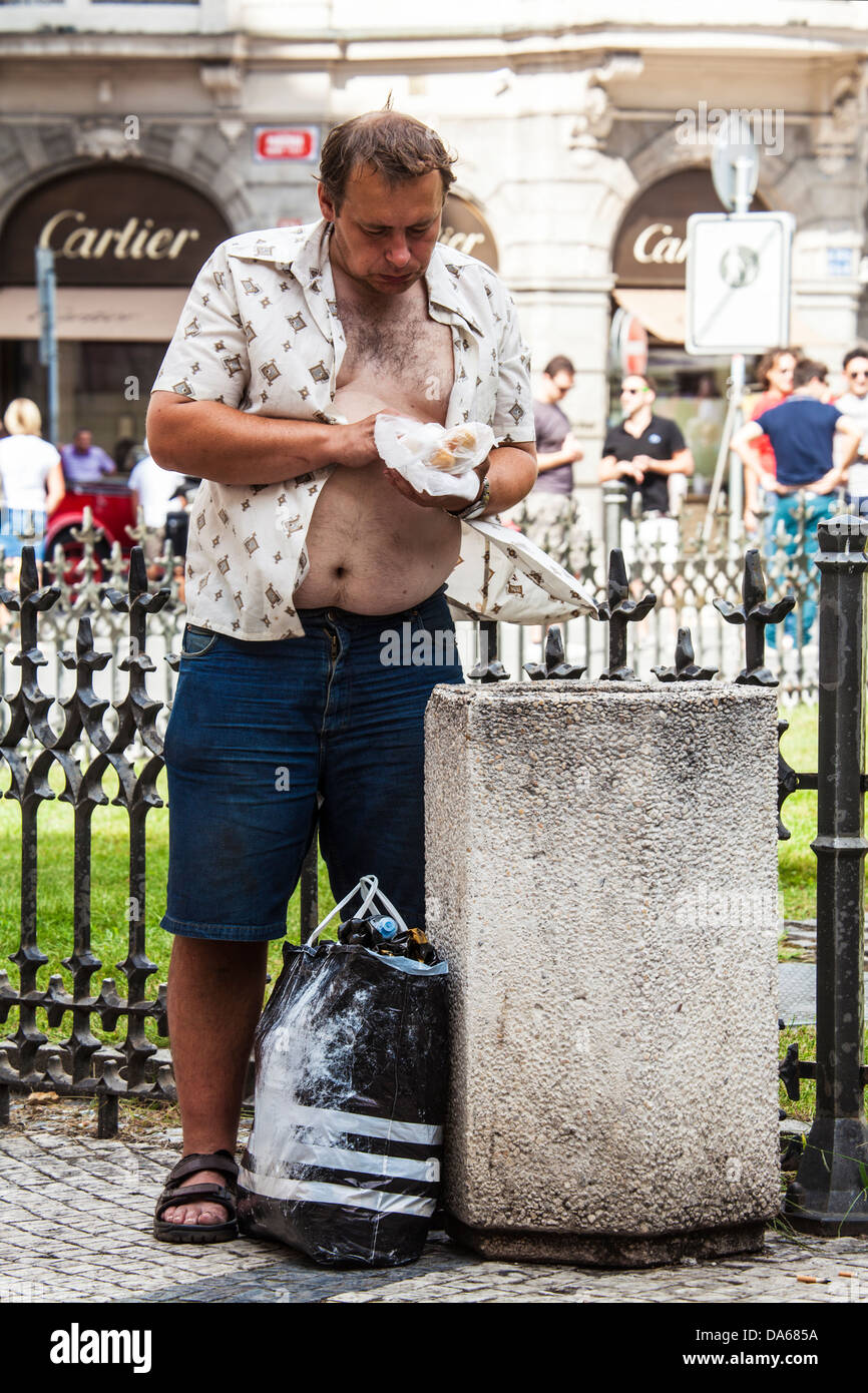 Un senzatetto uomo guarda attraverso la lettiera per alimenti in Town Square, Praga. Negozio di Cartier in background. Il contrasto della ricchezza e della povertà. Foto Stock