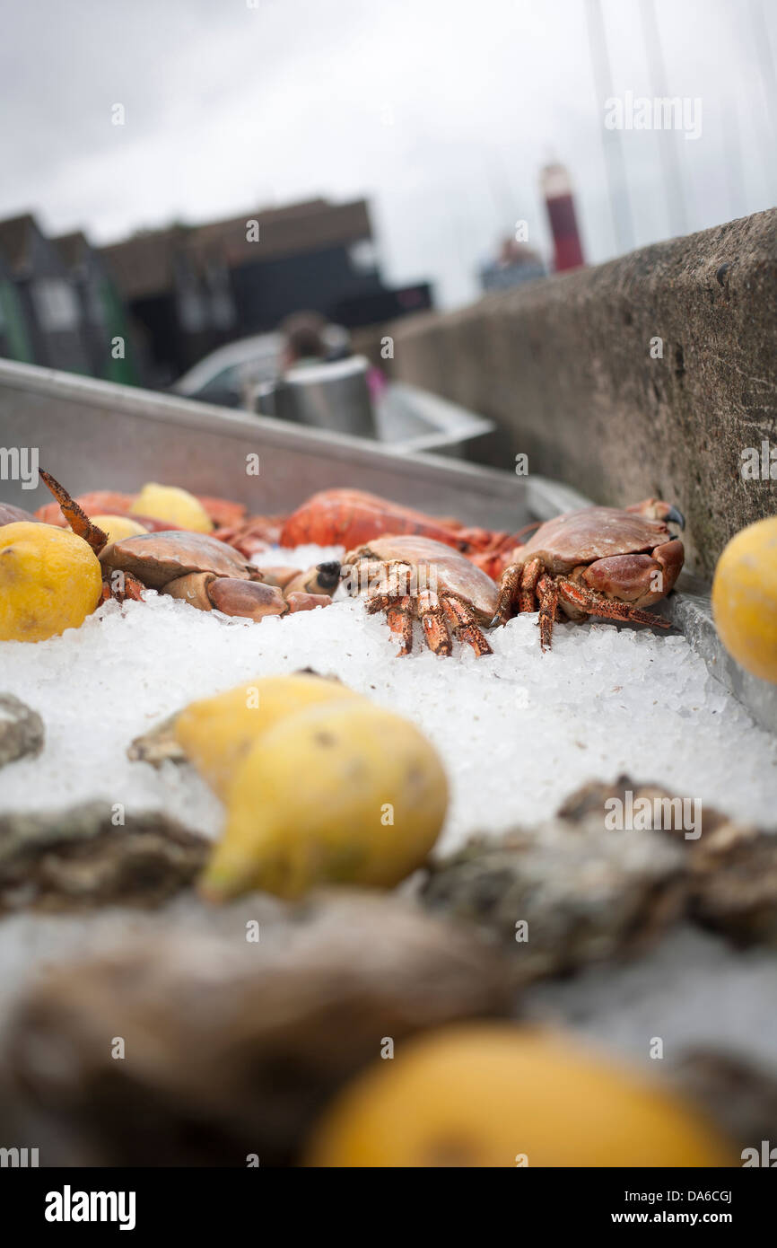 Granchi freschi, ostriche e gamberi su letto di ghiaccio con i limoni a beach cafe a Whitstable vicino alla parete del mare, con Fisherman's capanne Foto Stock