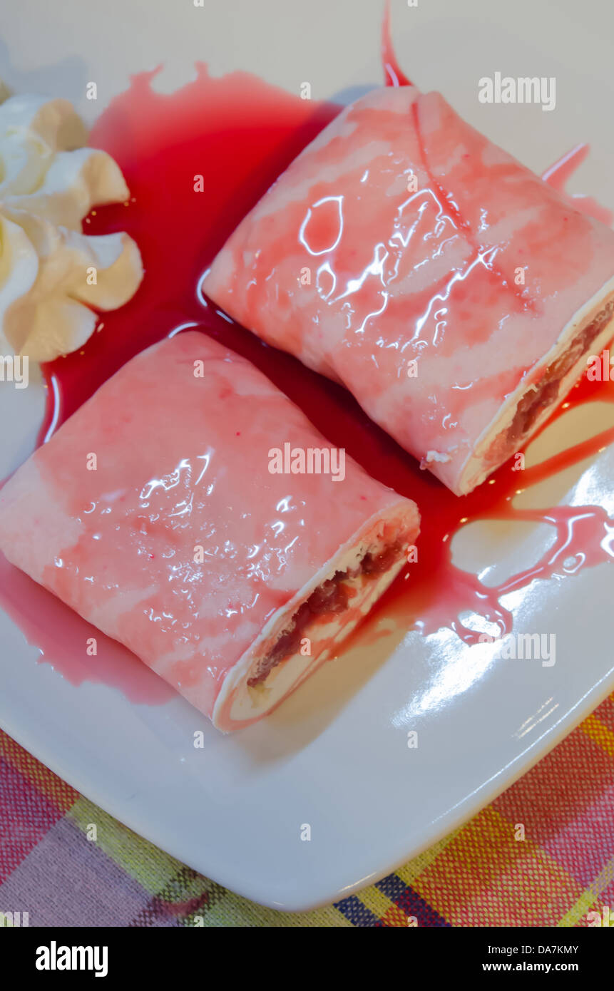 Viste dall'alto crêpe rotoli riempiti con crema bianca e fragole, guarnire con sciroppo di fragole servito con panna montata sul piatto Foto Stock