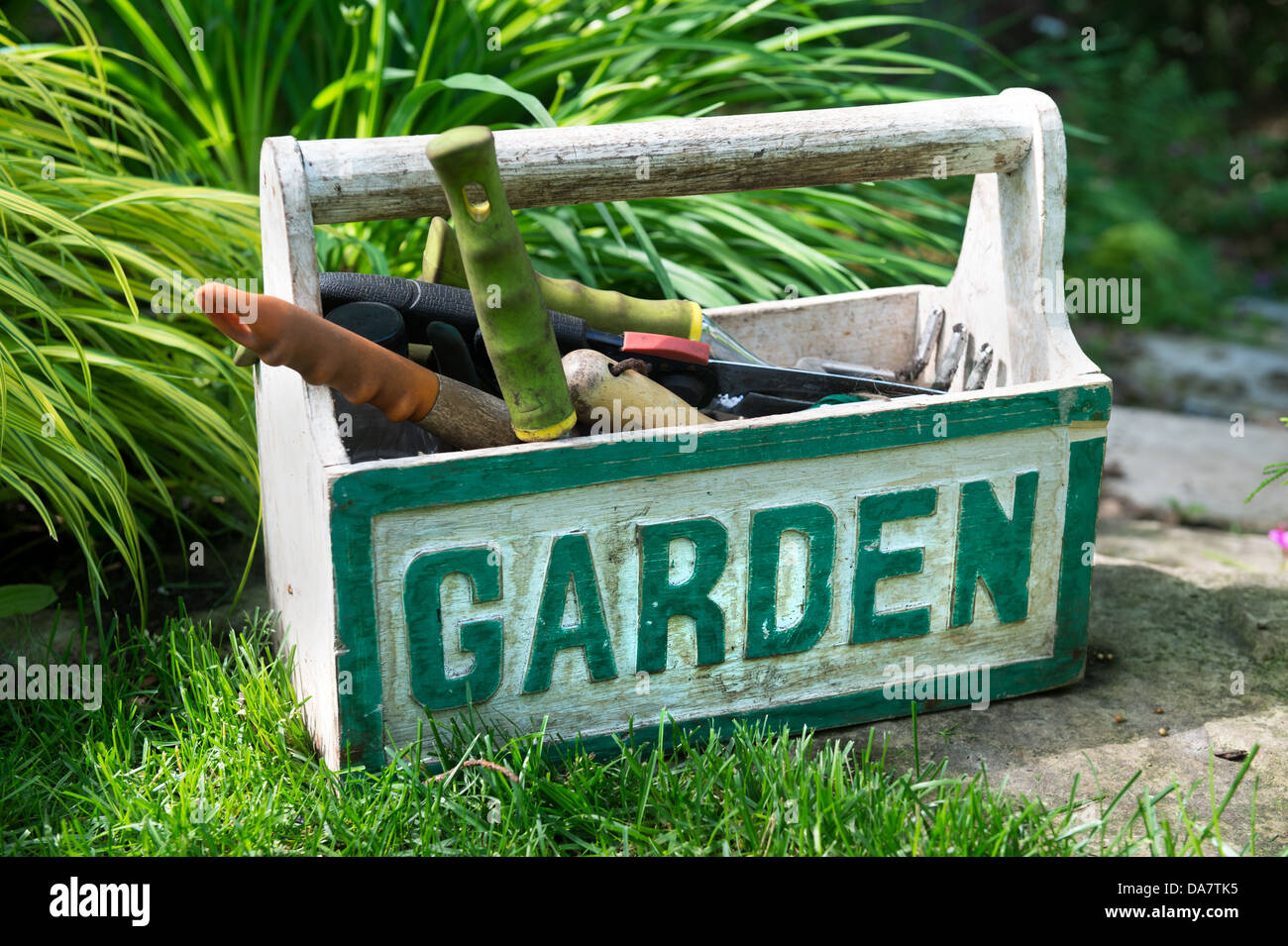 Una scatola con la parola 'Garden' riempito con utensile da giardinaggio seduti in giardino Foto Stock