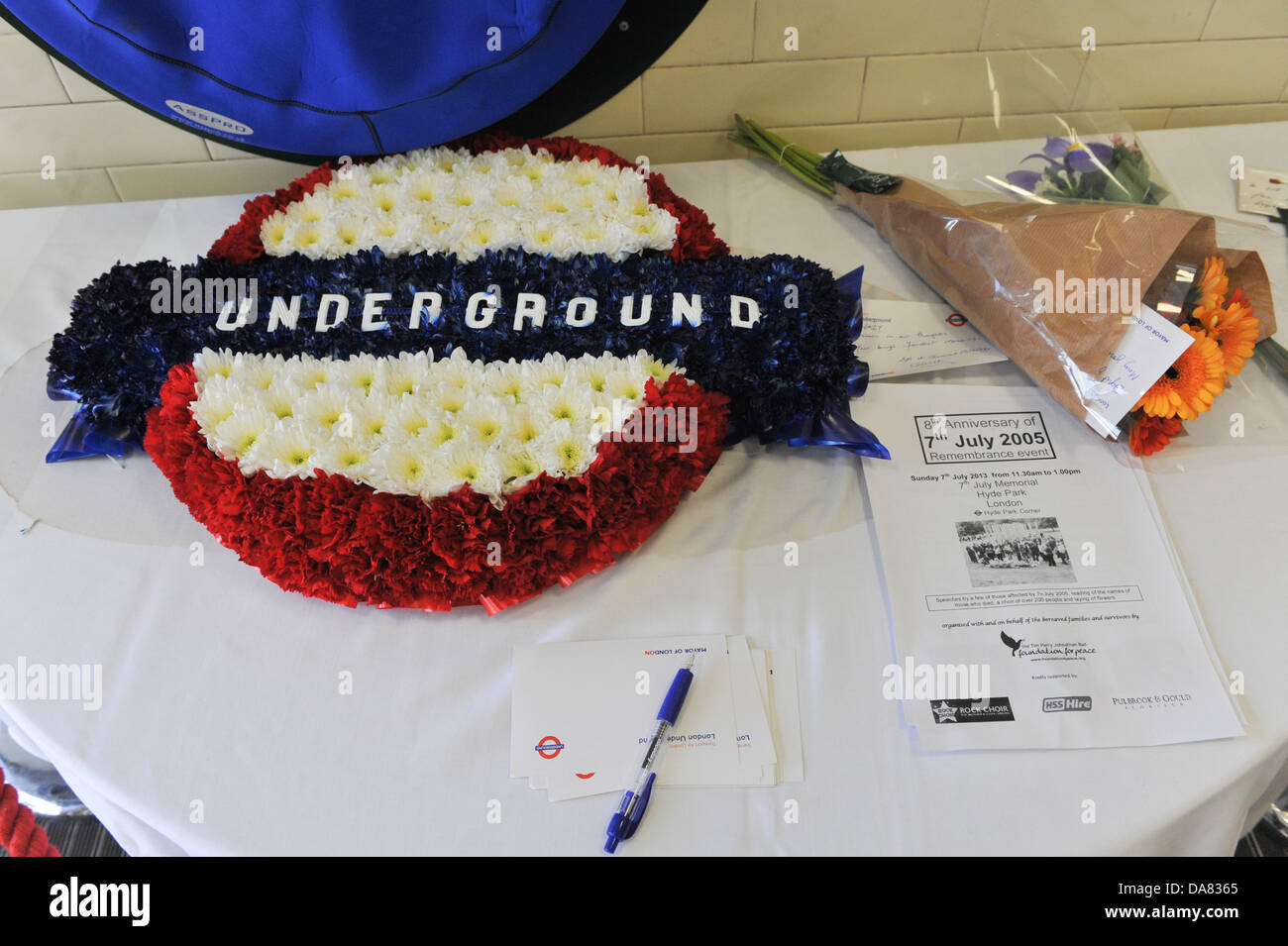 La stazione della metropolitana di Russell Square, Londra, Regno Unito. Il 7 luglio 2013. Fiori e ghirlande di cui sotto la lapide commemorativa di coloro che sono morti o sono stati feriti durante i bombardamenti terroristici. Foto Stock