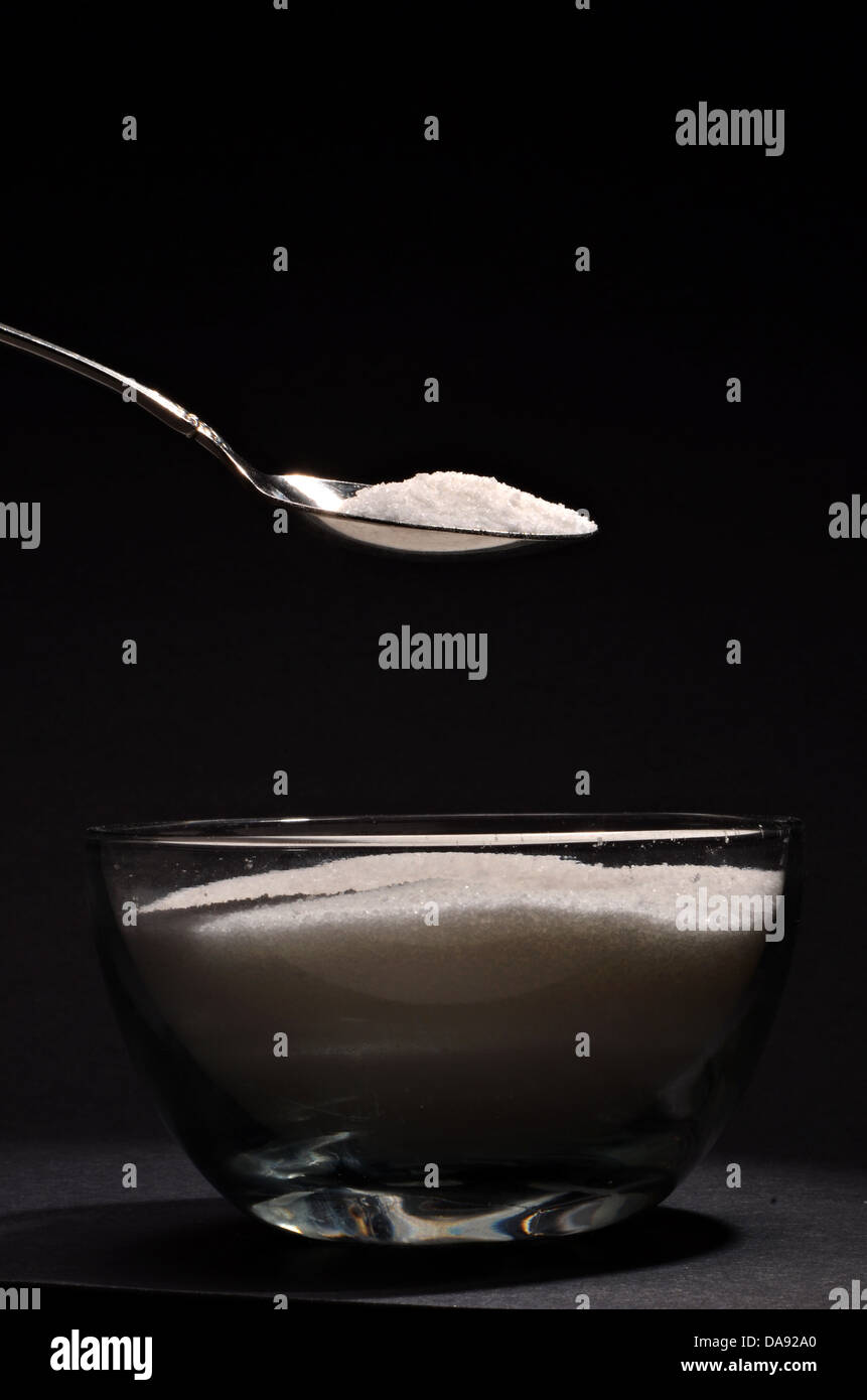 Un cucchiaio pieno di zucchero è su una tazza di zucchero Foto Stock