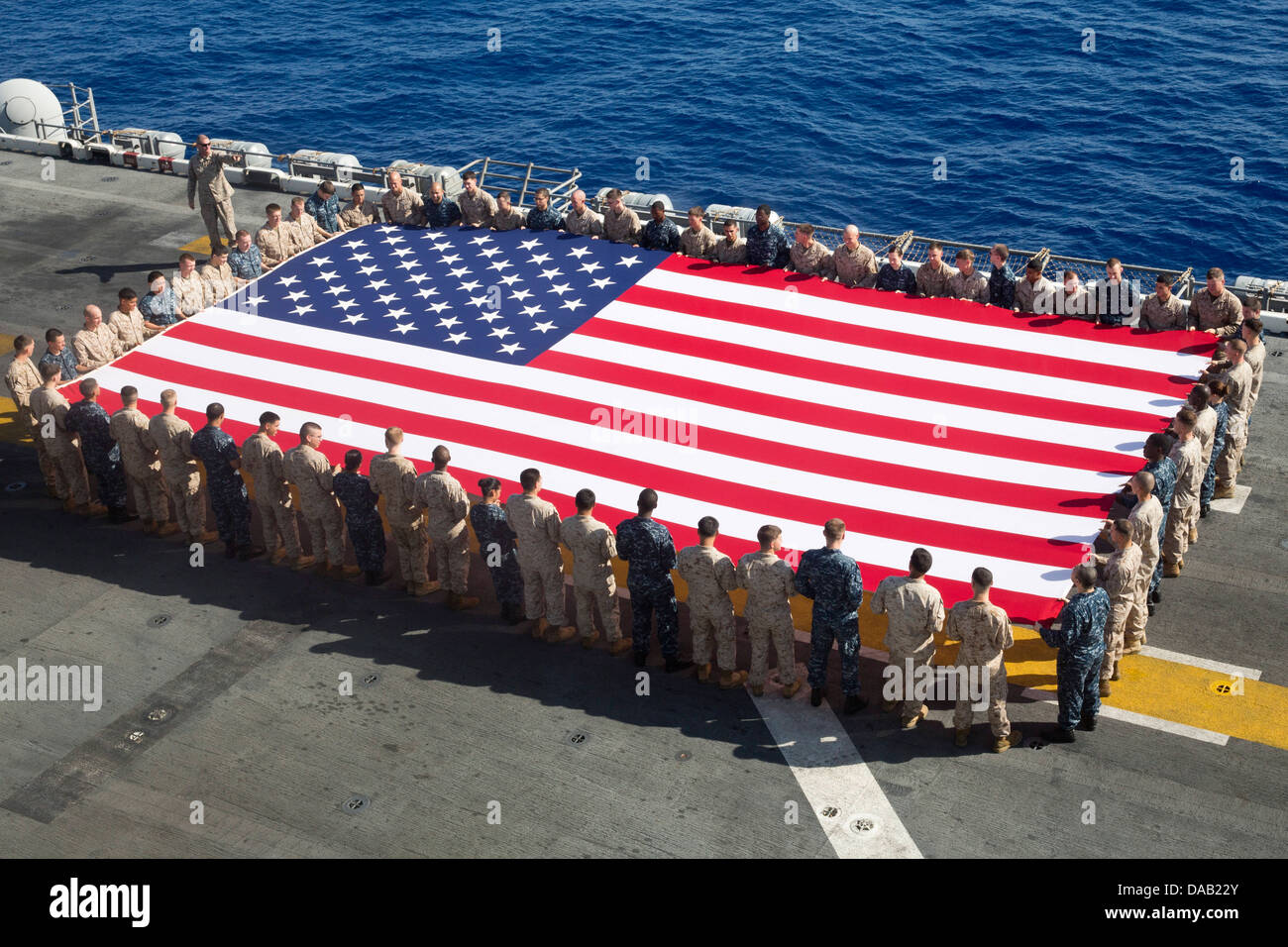 Marinai e Marines visualizzare il ensign nazionale in onore del giorno di indipendenza a bordo dell'assalto anfibio nave USS Kearsarge (LHD 3). Kearsarge è l'ammiraglia per il Kearsarge Amphibious pronto il gruppo e con la avviato 26 Marine Expeditionary Unit Foto Stock