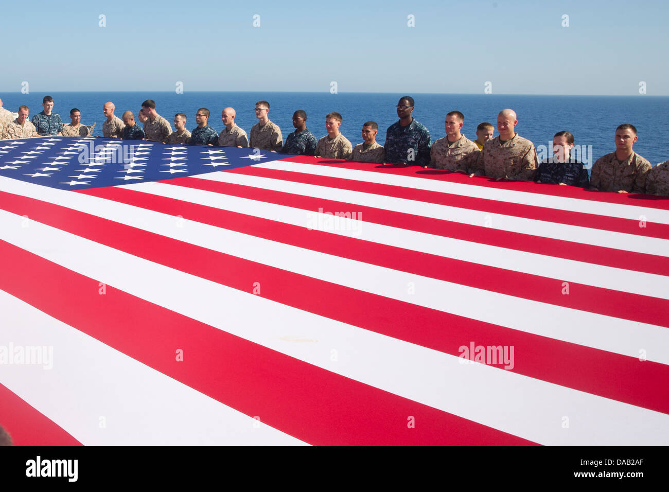 Marinai e Marines visualizzare il ensign nazionale in onore del giorno di indipendenza a bordo dell'assalto anfibio nave USS Kearsarge (LHD 3). Kearsarge è l'ammiraglia per il Kearsarge Amphibious pronto il gruppo e con la avviato 26 Marine Expeditionary Unit Foto Stock