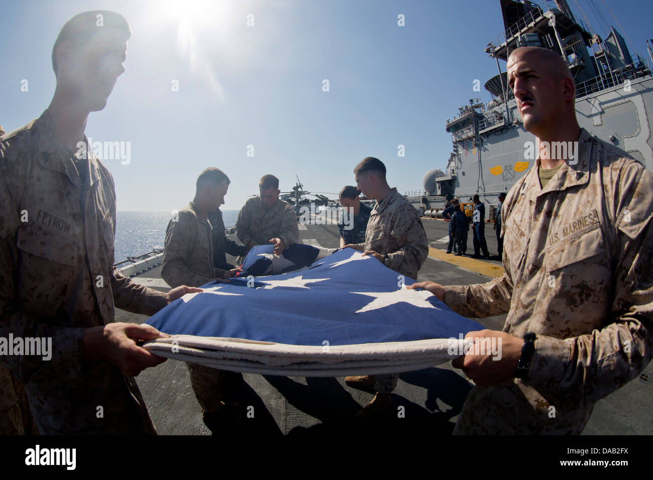 Marinai e Marines piegare il ensign nazionale dopo la visualizzazione sul ponte di volo in onore del giorno di indipendenza a bordo della amp Foto Stock