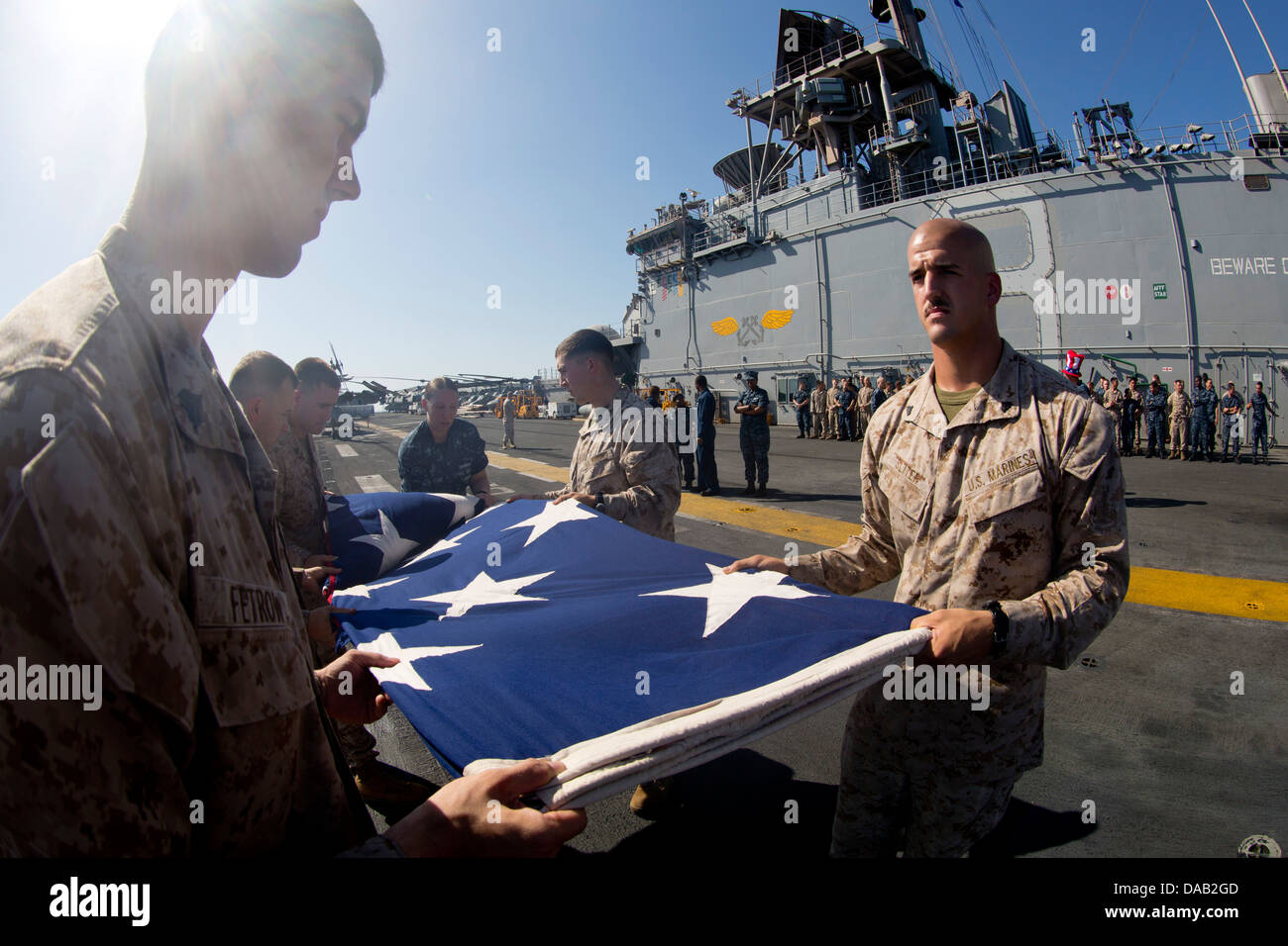 Marinai e Marines piegare il ensign nazionale dopo la visualizzazione sul ponte di volo in onore del giorno di indipendenza a bordo della amp Foto Stock