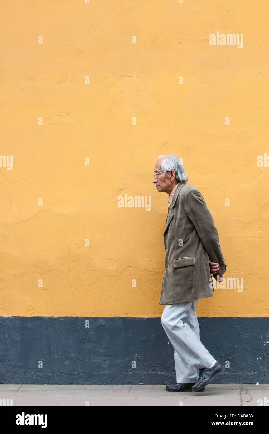 Anziani vecchio uomo a camminare sul marciapiede accanto a orange Wall Street scene downtown Trujillo, Perú.anziani Foto Stock