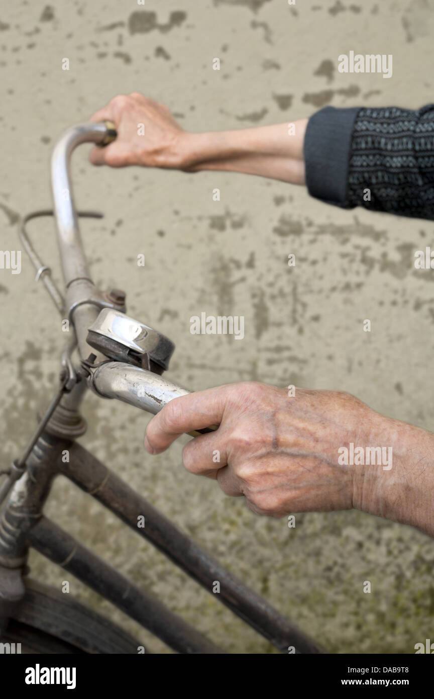Anziani mani tenendo il manubrio di una bicicletta. Messa a fuoco selettiva con profondità di campo ridotta. Foto Stock