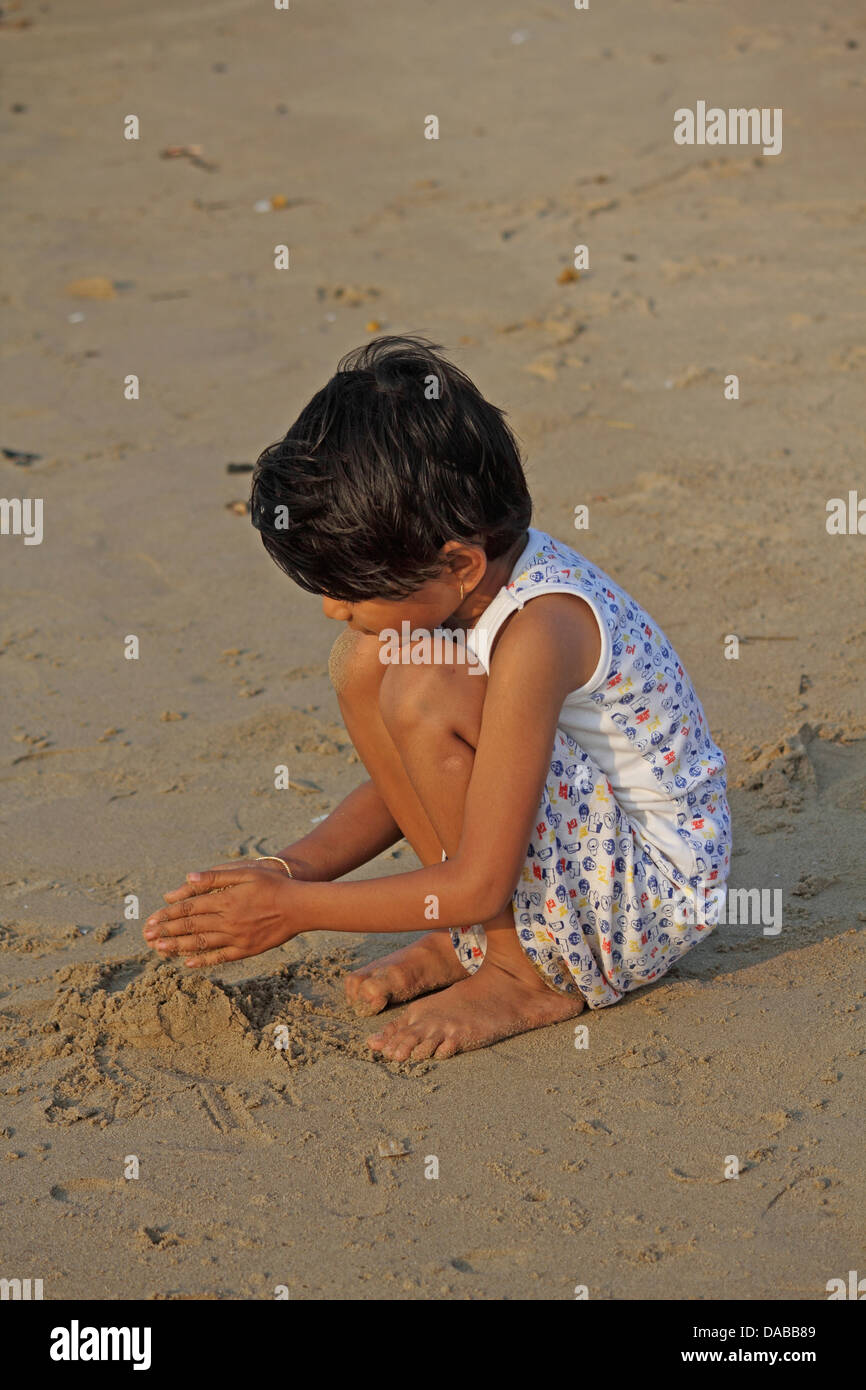 Piccola ragazza che gioca nella sabbia sulla spiaggia, Goa, India Foto Stock