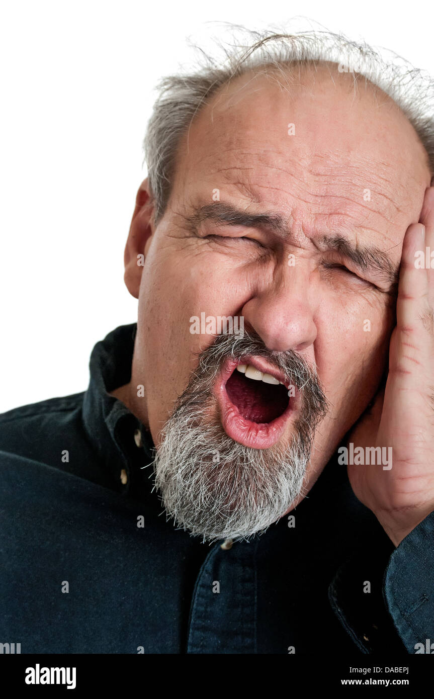 Balding l uomo nella sua anni sessanta tenendo la sua testa nel dolore come egli grida. Isolato su uno sfondo bianco. Foto Stock