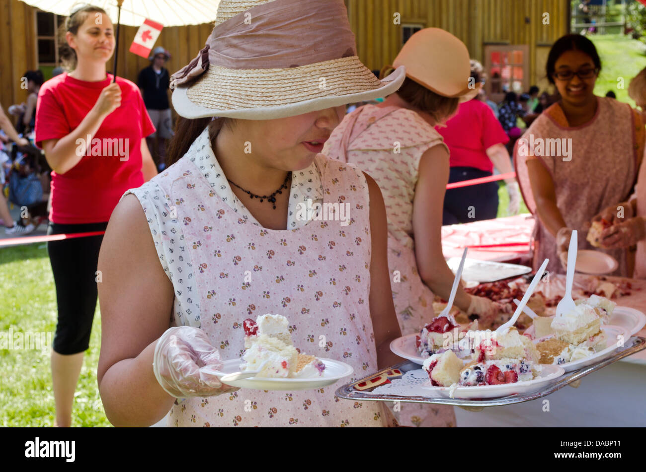 Donna volontario nel 1920s costume mette la torta di compleanno sul Canada Il giorno 1 luglio 2013 a Burnaby Village Museum. Foto Stock
