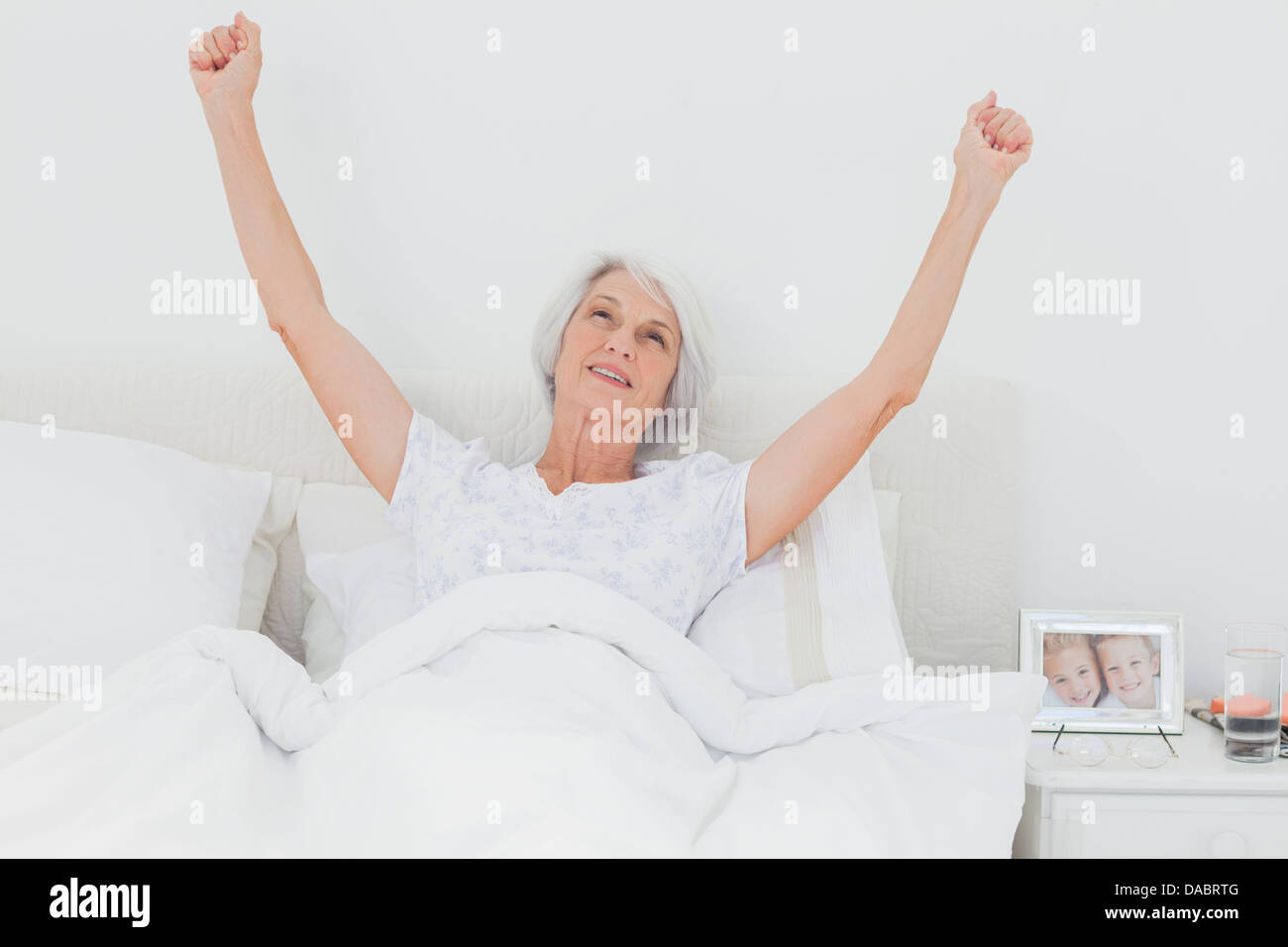 Donna di svegliarvi e bracci di sollevamento a letto Foto Stock