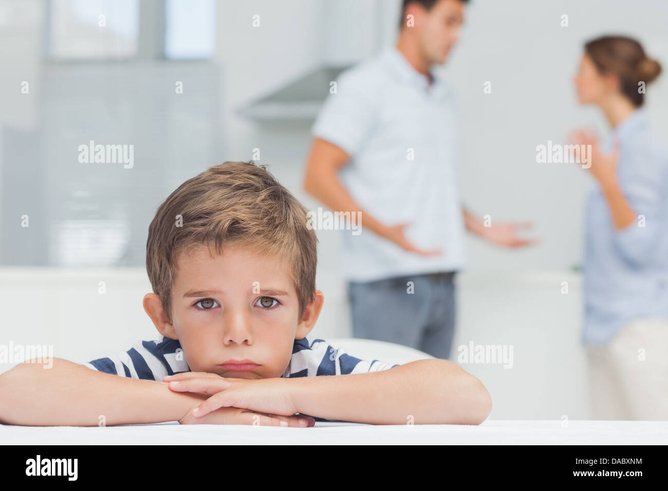 Triste ragazzo con le braccia incrociate mentre i genitori quarreling Foto Stock
