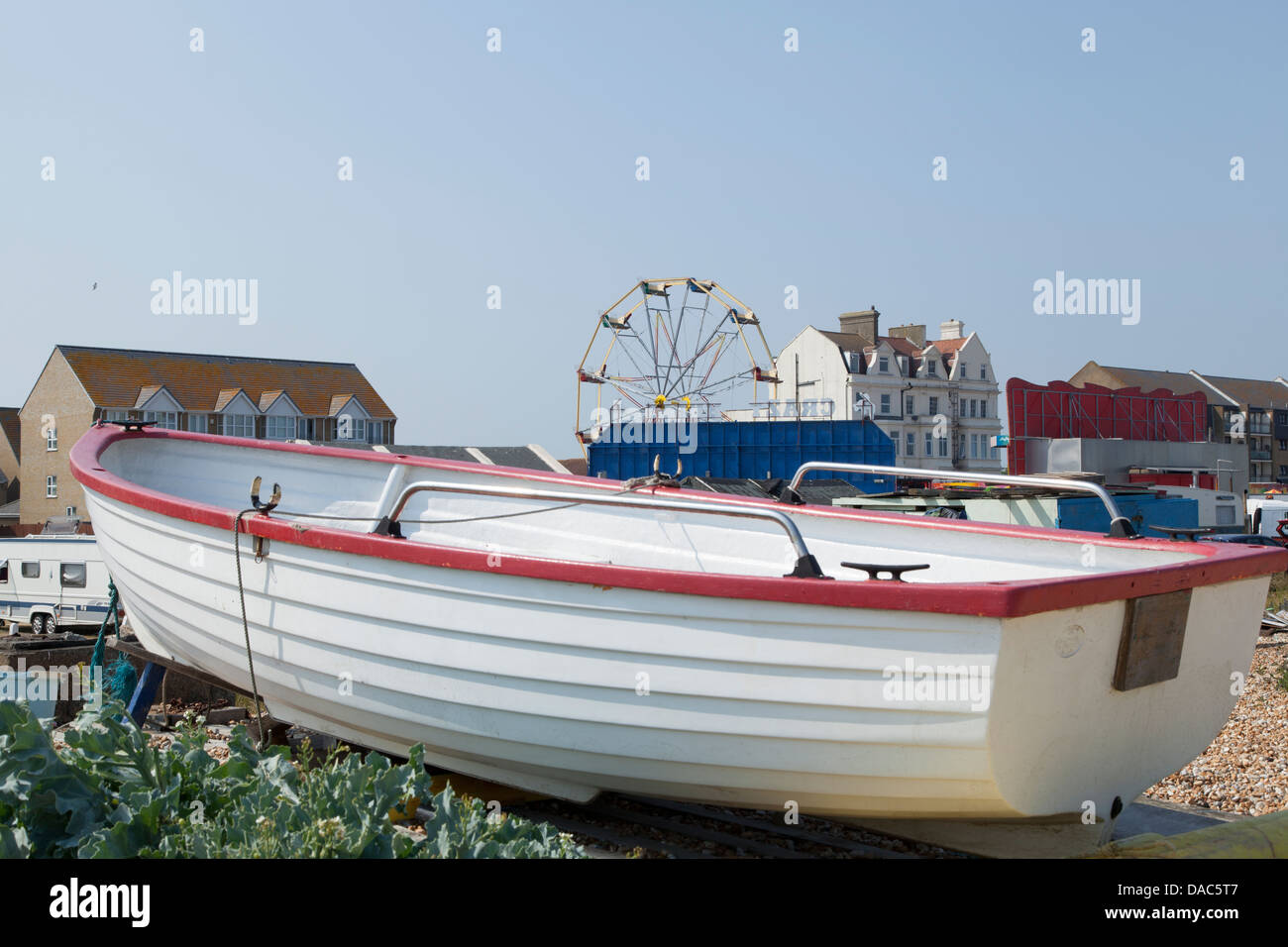 Bianco barca di legno in primo piano in riva alla spiaggia con ruota panoramica Ferris in background Foto Stock