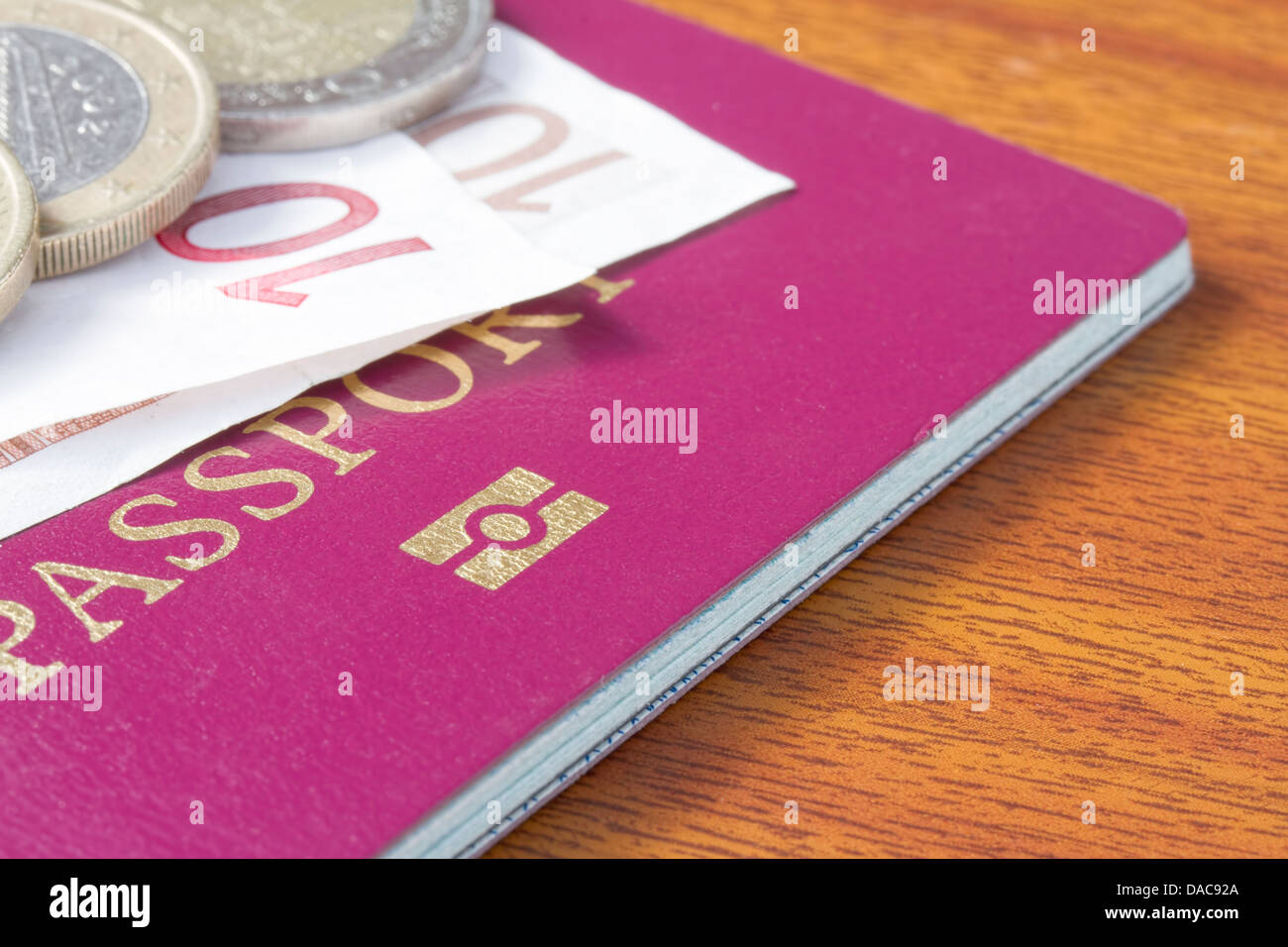 Passaporto britannico con monete e banconote in euro sulla tavola di legno Foto Stock