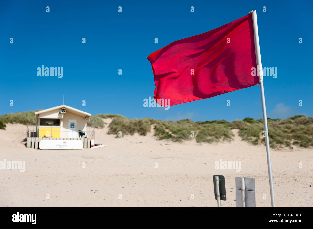 Una bandiera rossa battenti nella parte anteriore di un bagnino post a Constantine Bay beach Cornwall Regno Unito Foto Stock