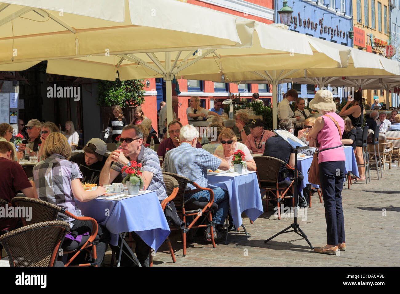 Occupato ristoranti e caffetterie all'aperto con le persone per cenare fuori sotto gli ombrelloni sulla strada in estate. Nyhavn Copenaghen Zelanda Danimarca Foto Stock