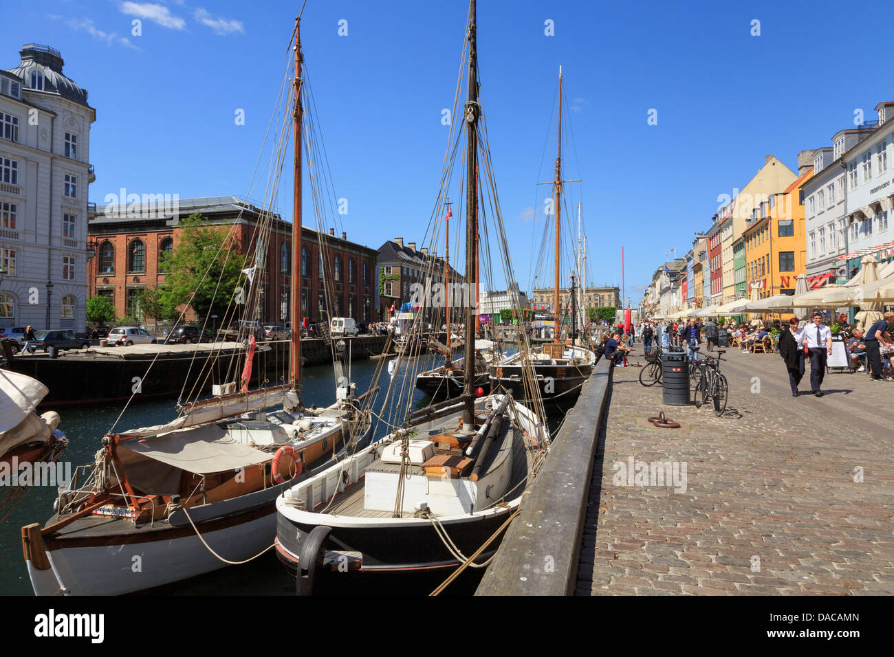 Vecchie barche ormeggiate sul canal dal lungomare pedonale strada con caffè all'aperto a Nyhavn, Copenaghen, Zelanda, Danimarca Foto Stock